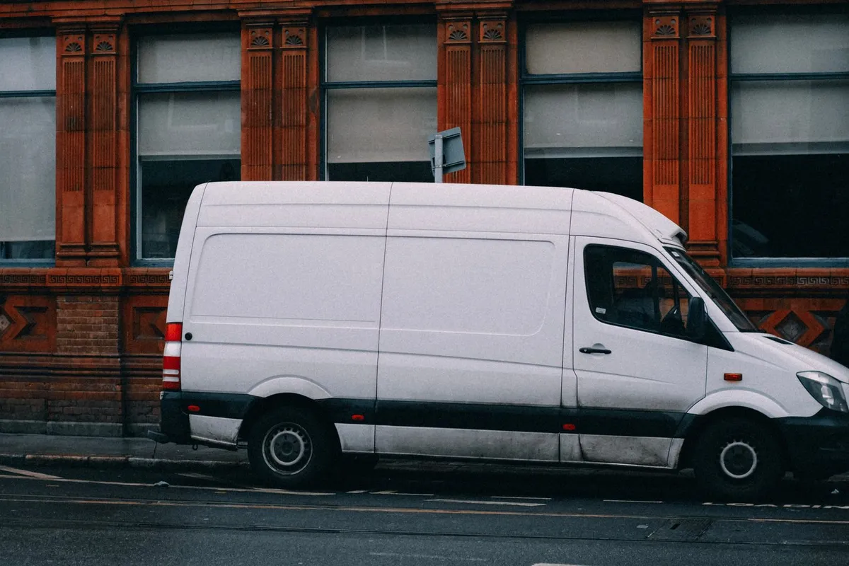Weißer Transporter ohne Beschriftung parkt in Seitenansicht an einer Stadtstraße vor einer roten Backsteinfassade