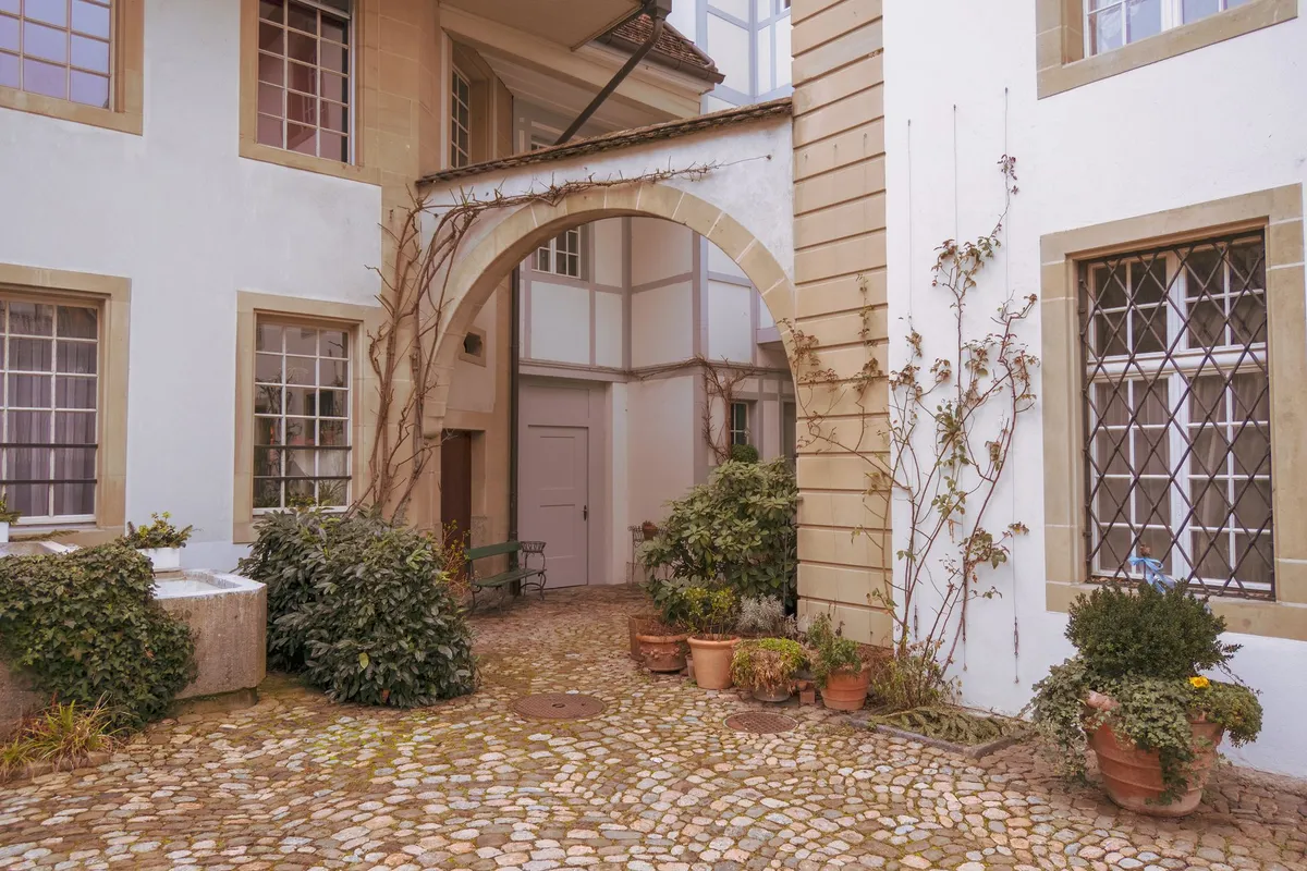 Gepflasterter Altstadthof mit Sandsteintorbogen, Fachwerkgiebel im Hintergrund und Tontöpfen mit Pflanzen am Hauseingang